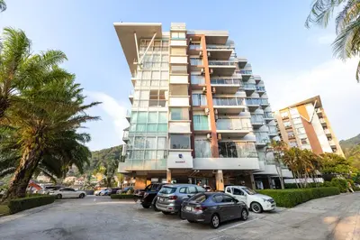 a tall building with cars parked in a parking lot at Sunset Residence Karon Beach in Karon Beach